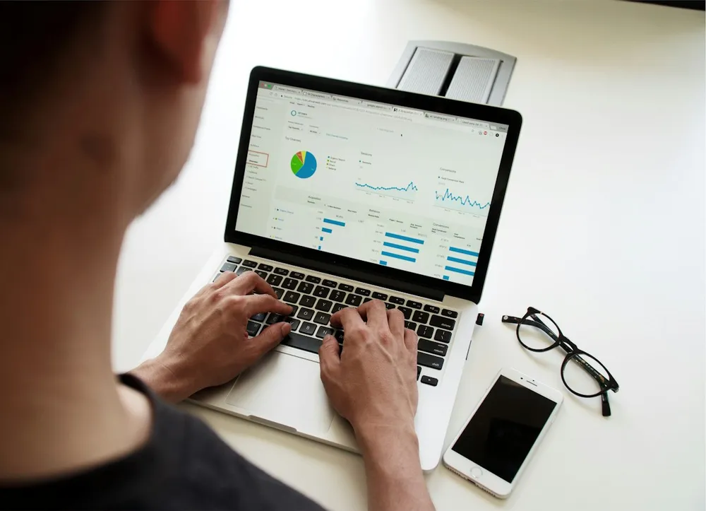 Marketer working on a laptop showing an analytics dashboard with charts